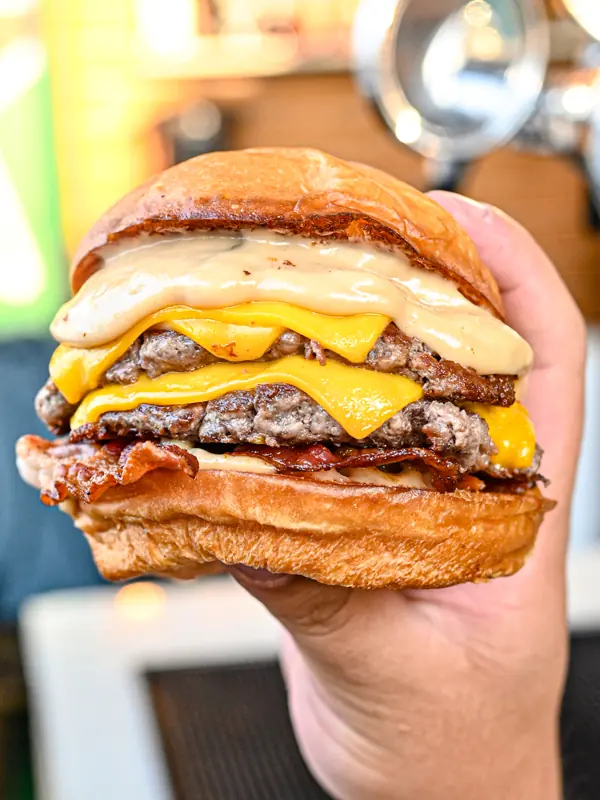 Hamburguesa doble con queso y salsa, sostenida en la mano